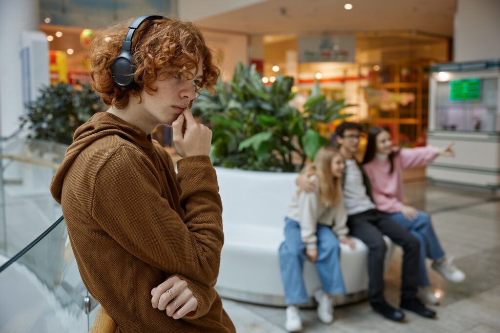 Portrait of sad serious teenager guy wearing headphones alone at shopping mall